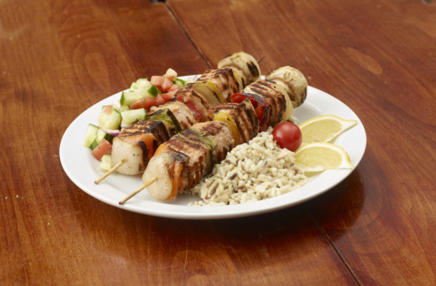 Salmon and Grilled Vegetable Kebabs with Wild Rice and a Diced Cucumber and Tomato Salad on a White Ceramic Dish on a Wooden Table
