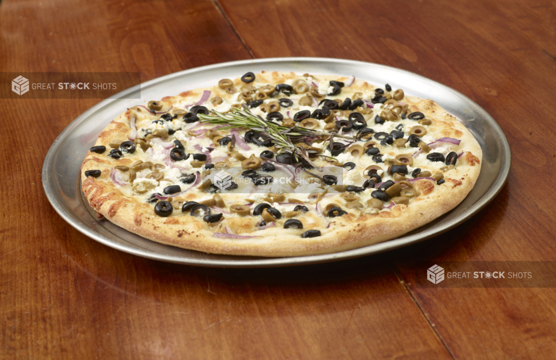 A Whole Mediterranean-Style Pizza with Red Onions, Feta Cheese and Olives on a Silver Platter on a Wooden Table