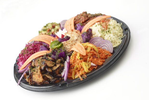 Middle Eastern appetizer platter with assorted grilled vegetables, salads and dips on a black round plastic catering tray