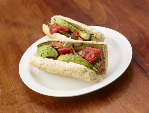 Vegetarian Sub Sandwich with Avocados, Grilled and Roasted Vegetables on Whole Wheat Bread, Sliced in Half on a White Ceramic Dish