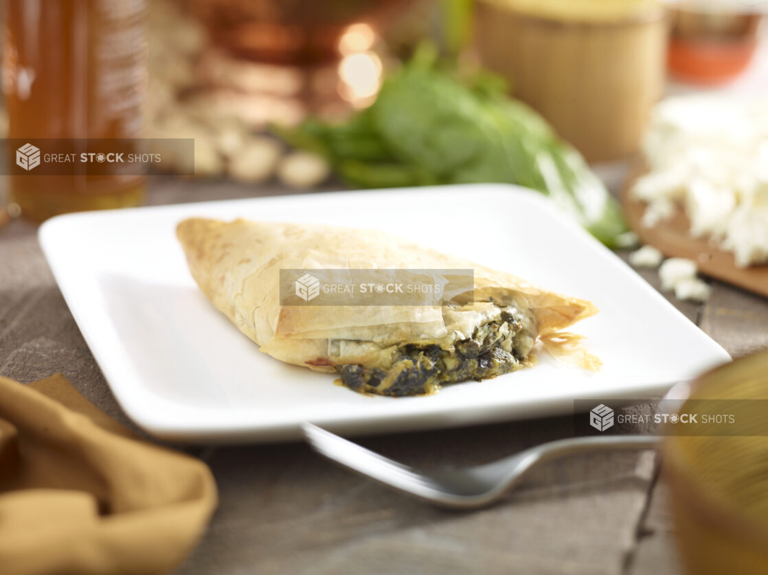 Spanakopita, spinach and cheese pie, on a square white side plate with a fork and napkin in a close up view