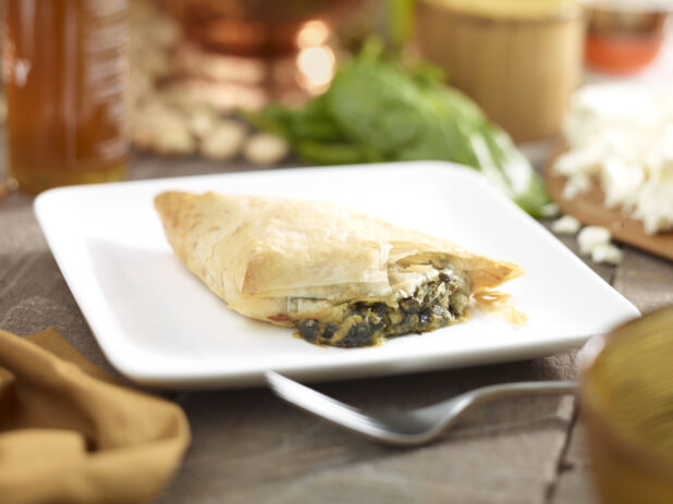 Spanakopita, spinach and cheese pie, on a square white side plate with a fork and napkin in a close up view