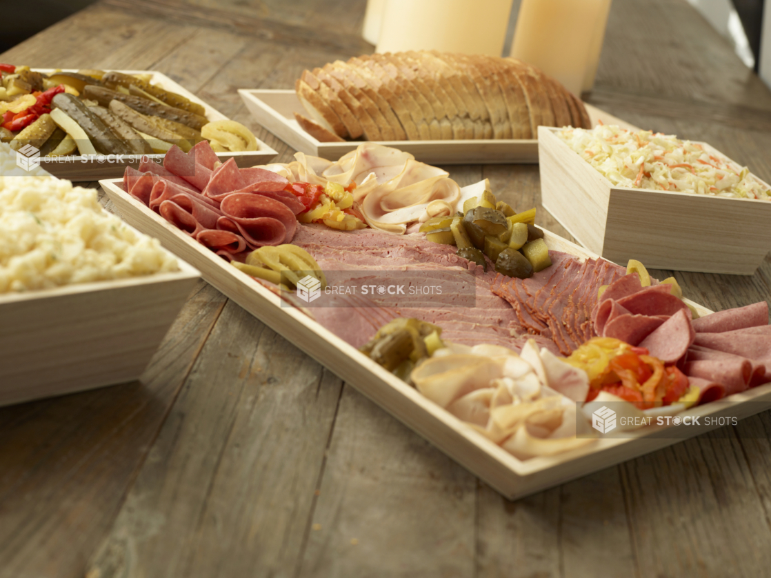 A Build Your Own Deli Sandwich Catering Package with Sliced Deli Meats, Rye Bread, Pickles and Side Salads in Wood Serving Trays