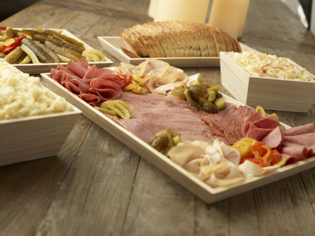 A Build Your Own Deli Sandwich Catering Package with Sliced Deli Meats, Rye Bread, Pickles and Side Salads in Wood Serving Trays