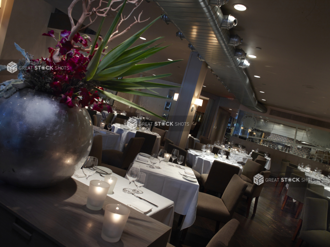 Interior of an elegant restaurant, tables set with white tablecloths and wine glasses, angled shot