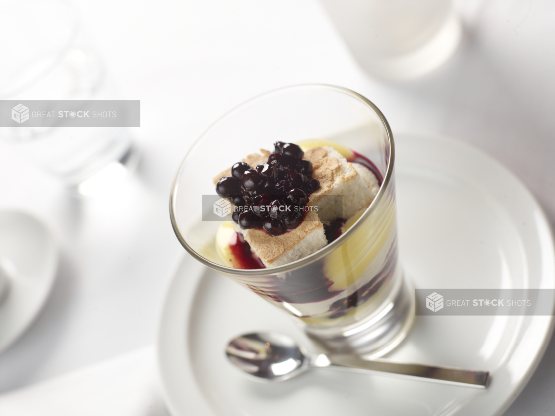 Blueberry Parfait with Custard and Whipped Cream and Berry Coulis in a Glass Cup on a White Ceramic Dish in a Fine Dining Setting