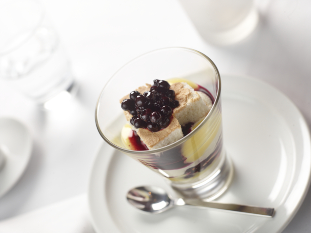 Blueberry Parfait with Custard and Whipped Cream and Berry Coulis in a Glass Cup on a White Ceramic Dish in a Fine Dining Setting