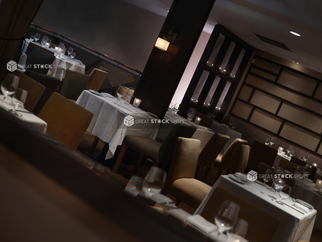 Interior of an elegant restaurant, tables set with white tablecloths and wine glasses, angled shot