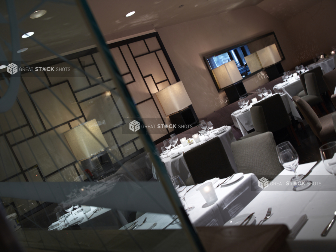 Interior of an elegant restaurant, tables set with white tablecloths and wine glasses, angled shot