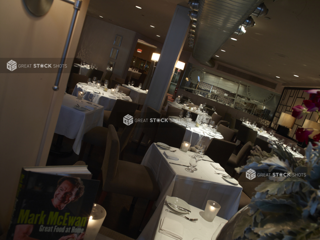 Interior of an elegant restaurant, tables set with white tablecloths and wine glasses, angled shot