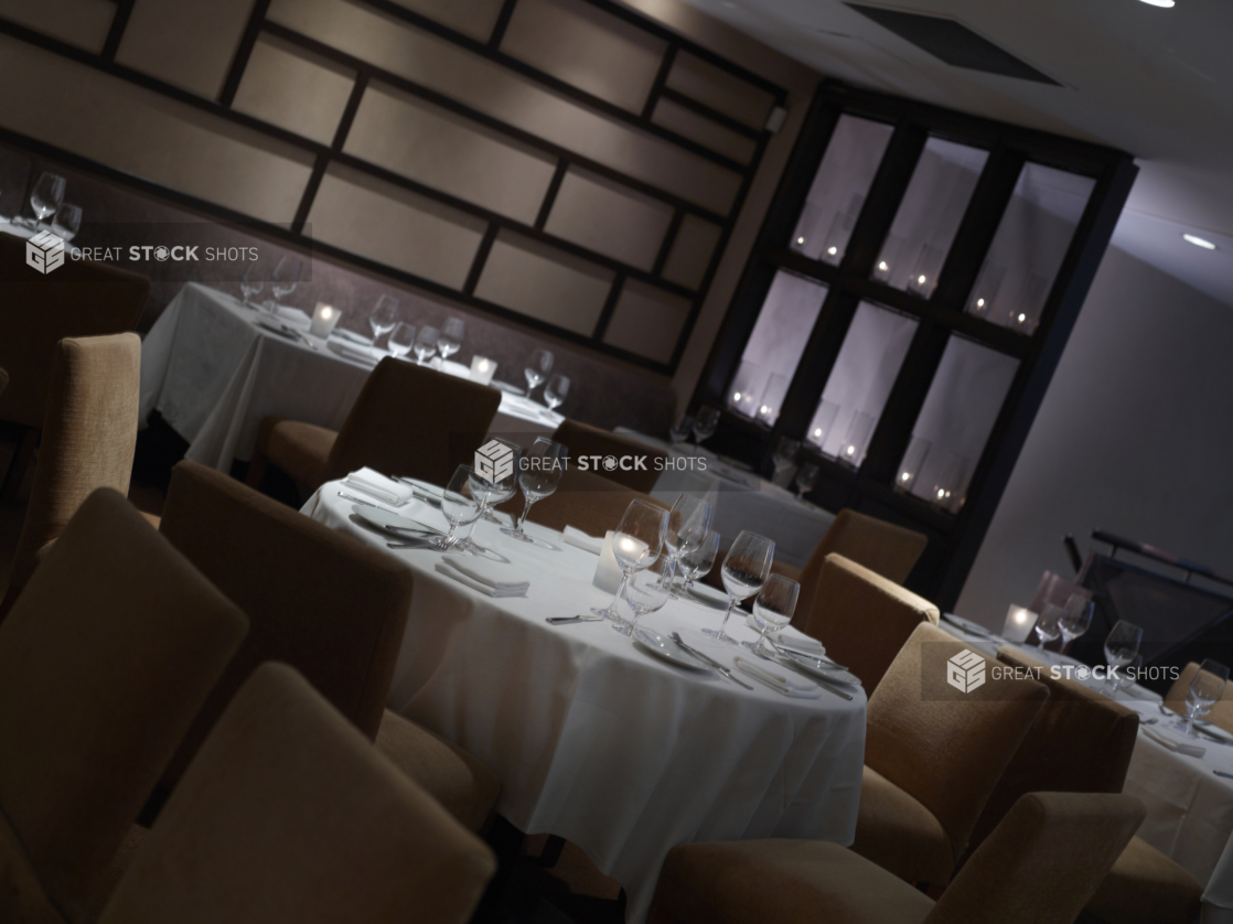 Interior of an elegant restaurant, tables set with white tablecloths and wine glasses, angled shot