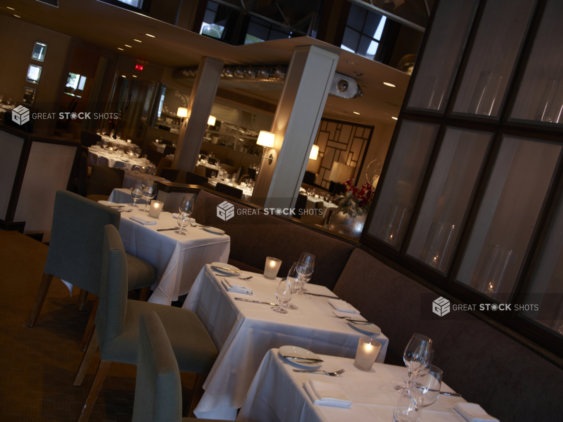 Interior of an elegant restaurant, tables set with white tablecloths and wine glasses, angled shot