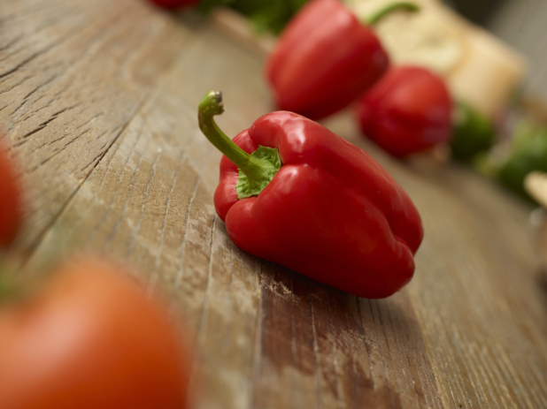 Close Up of a Fresh Whole Red Bell Pepper on a Weathered Wooden Table Surface in an Indoor Setting