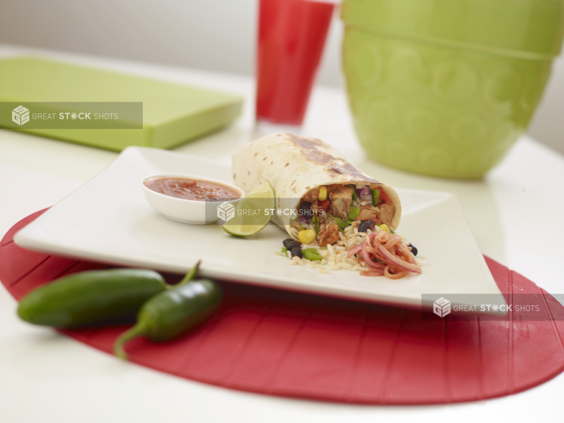 Shrimp burrito with a slice of lime and a ramekin of red salsa on a square white plate