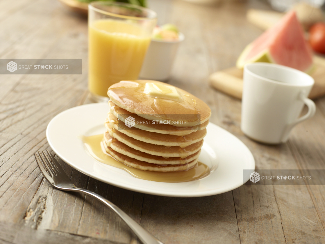 Stack of Mini Pancakes with a Pat of Butter and Maple Syrup on a White Ceramic Dish on a Rustic Wooden Table