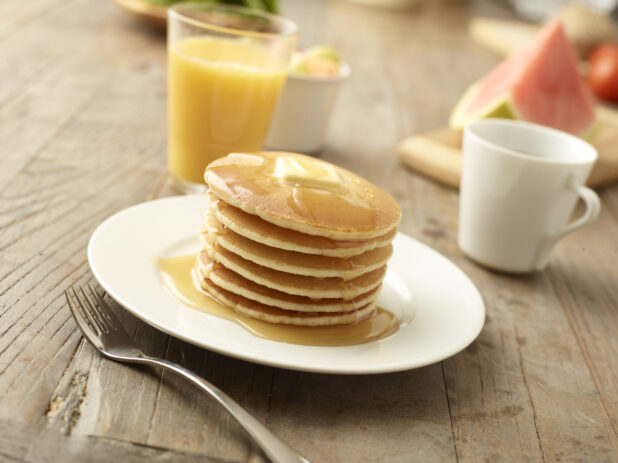 Stack of Mini Pancakes with a Pat of Butter and Maple Syrup on a White Ceramic Dish on a Rustic Wooden Table