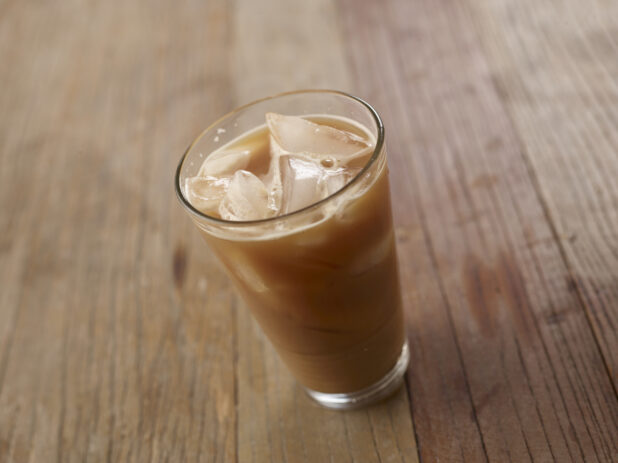 Close Up of a Glass Tumbler of Iced Cafe Latte with Ice Cubes on a Rustic Wooden Table