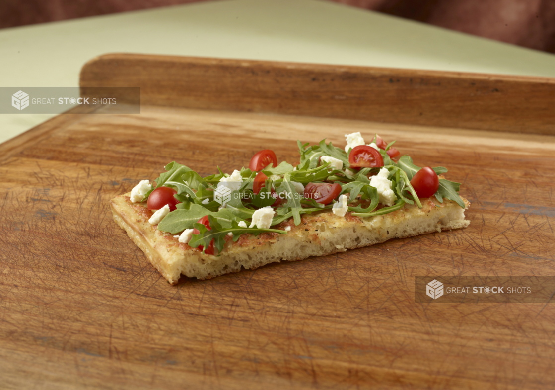 Focaccia with arugula, cherry tomatoes and feta on a wooden cutting board