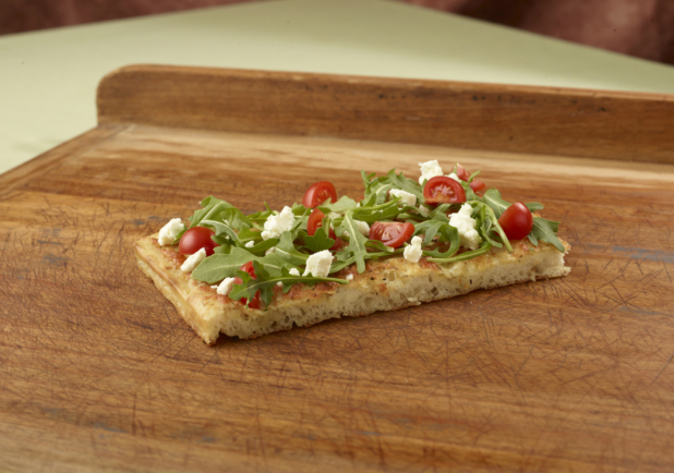 Focaccia with arugula, cherry tomatoes and feta on a wooden cutting board