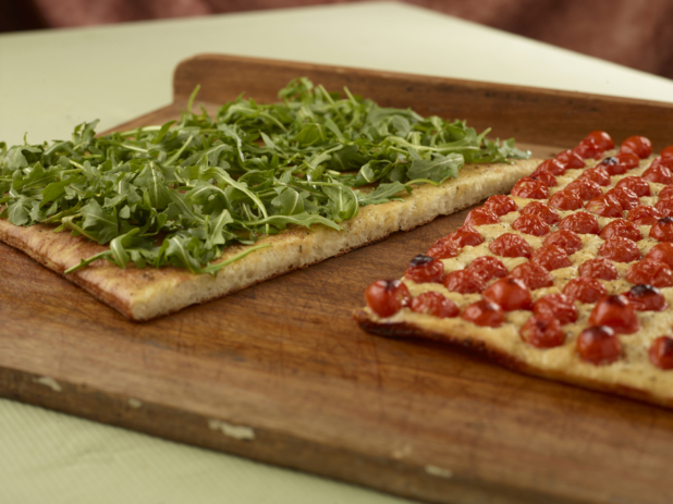 Close Up of a Cut Sicilian-Style Rectangular Pizza with Half Fresh Arugula and Half Blistered Tomato Toppings on a Wooden Board