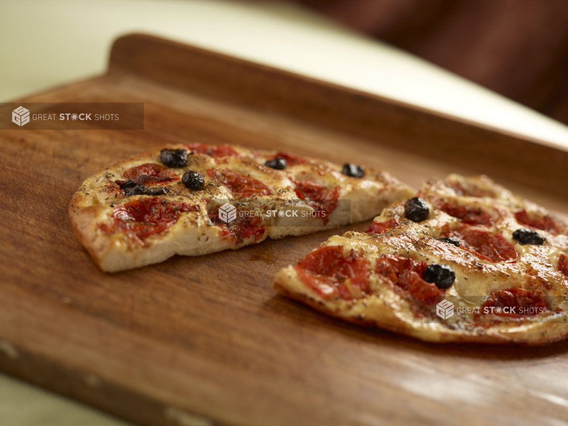 Round herbed cherry tomato and black olive flatbread cut in half on a wooden cutting board, close-up