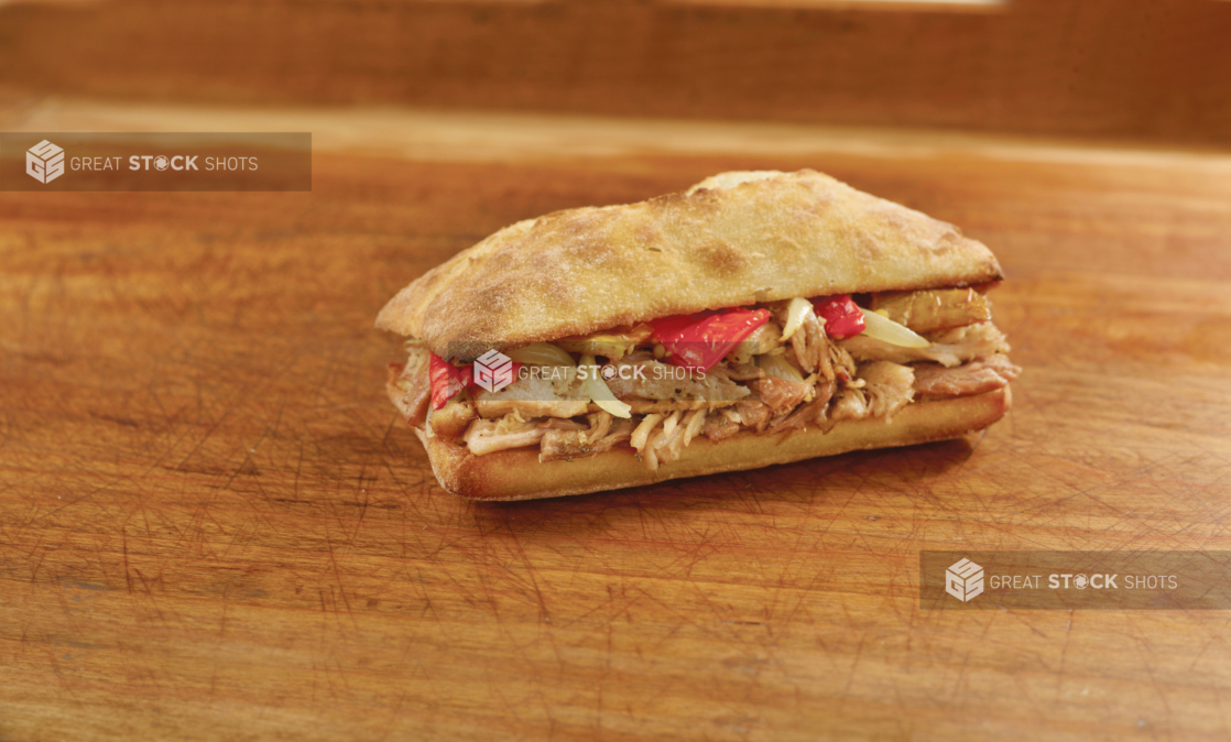 Pulled pork sandwich with roasted peppers on a panini bun, wood background