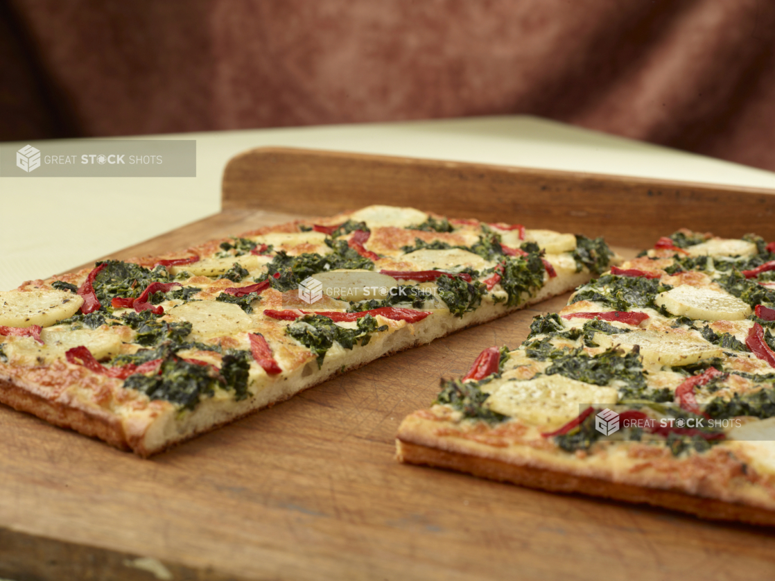 Close Up of a Cut Sicilian-Style Rectangular Pizza with Potato, Spinach and Roasted Red Pepper Toppings on a Wooden Board