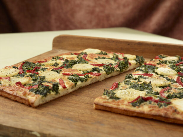 Close Up of a Cut Sicilian-Style Rectangular Pizza with Potato, Spinach and Roasted Red Pepper Toppings on a Wooden Board