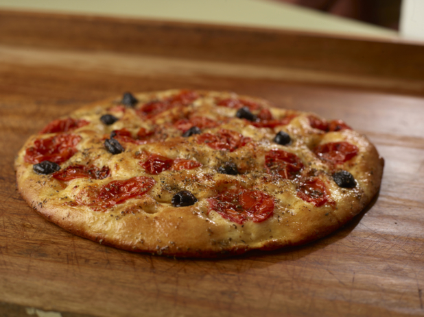 Round herbed cherry tomato and black olive flatbread on a wooden cutting board, close-up