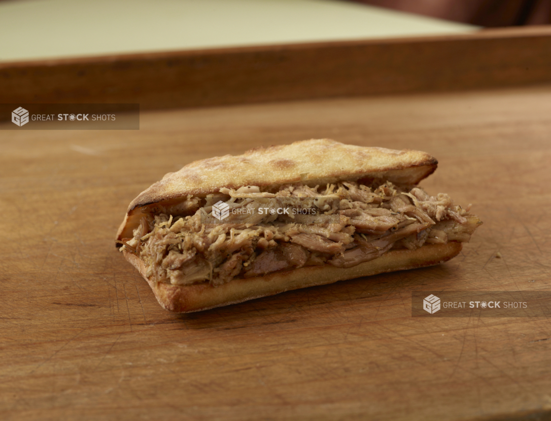 Pulled pork sandwich on a ciabatta bun, slightly open, on a wooden tabletop