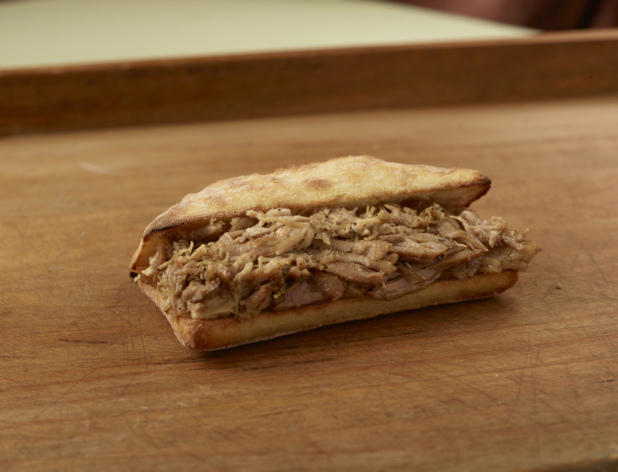 Pulled pork sandwich on a ciabatta bun, slightly open, on a wooden tabletop