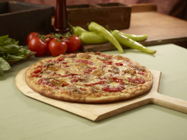 Whole unsliced pizza with pulled pork, roasted red peppers, and roasted garlic on a wood pizza peel with fresh vegetables in background, close-up, low angle