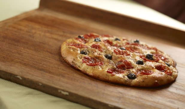 Round herbed cherry tomato and black olive flatbread on a wooden cutting board