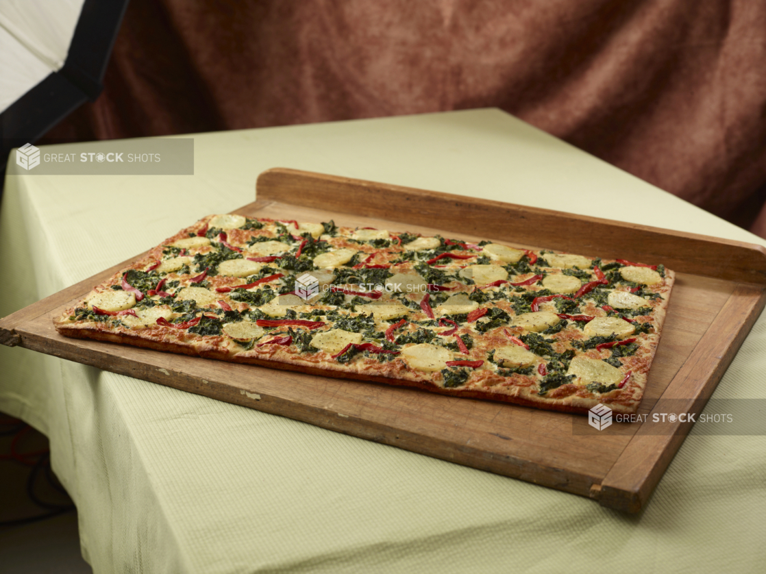 A Rectangular 3-Topping Party-Sized Pizza with Potatoes, Spinach and Red Pepper Toppings on a Wooden Board