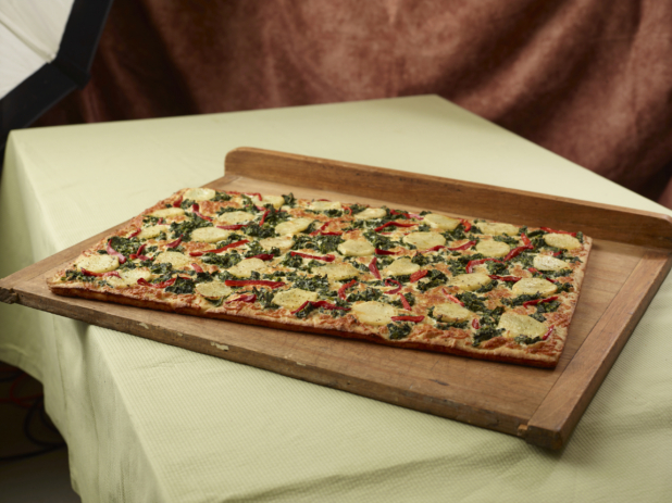 A Rectangular 3-Topping Party-Sized Pizza with Potatoes, Spinach and Red Pepper Toppings on a Wooden Board