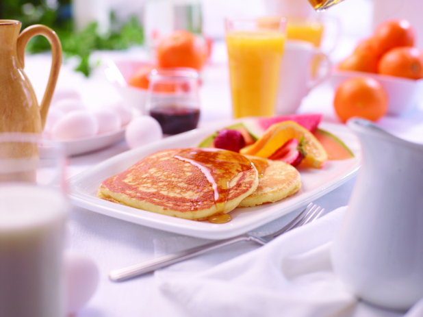 A Platter of Buttermilk Pancakes with Maple Syrup and Fresh Fruits on a White Dish in an Indoor Setting
