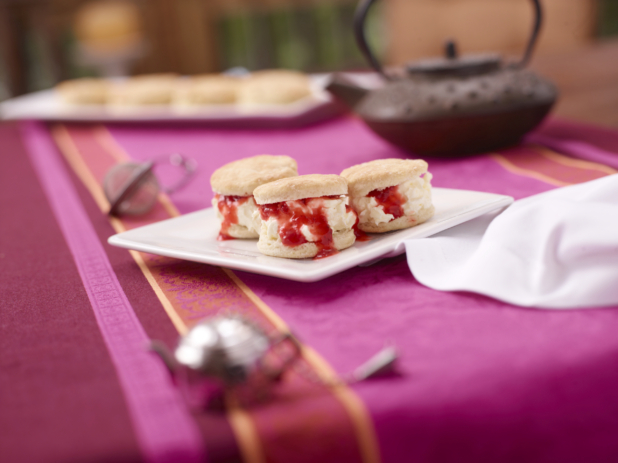 a close up of food on a aA Plate of Scone, Clotted Cream and Strawberry Jam Sandwiches on a Pink and Red Table Cloth Surfacetable