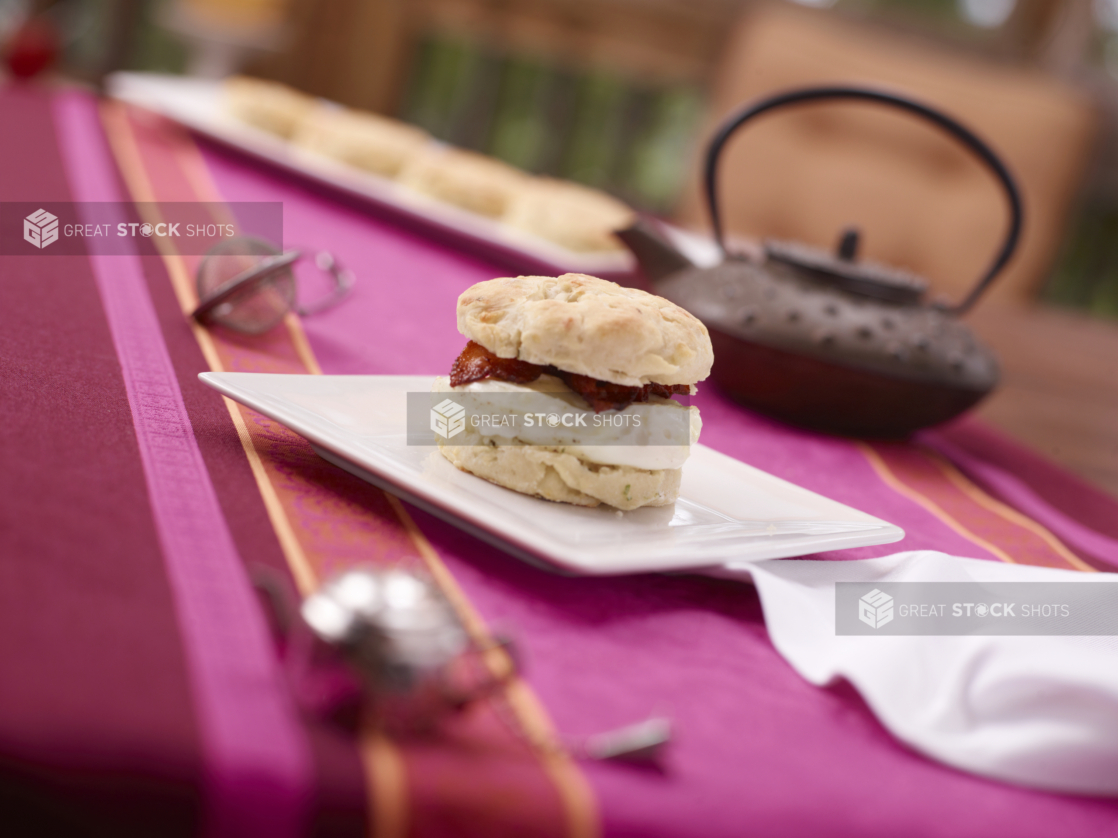 Breakfast Biscuit Sandwich with Egg Whites and Bacon on a White Ceramic Dish on a Pink and Red Table Cloth Surface
