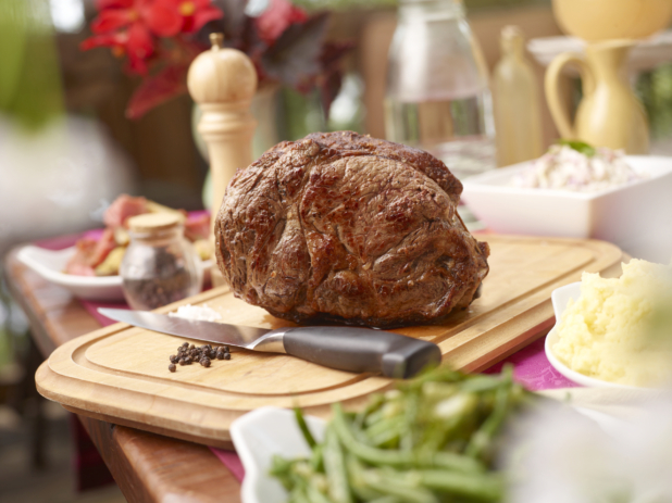 Whole roast of beef on a wood cutting board and kitchen knife on a buffet table