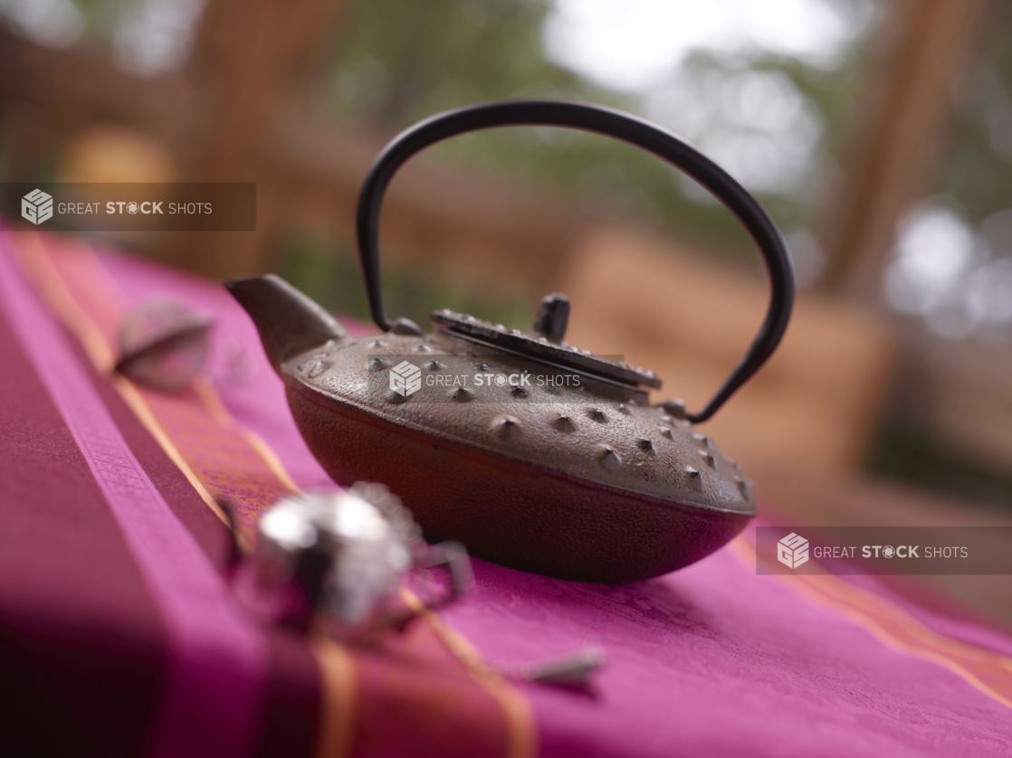 Japanese cast iron teapot on a bright pink tablecloth, shallow DOF, close-up