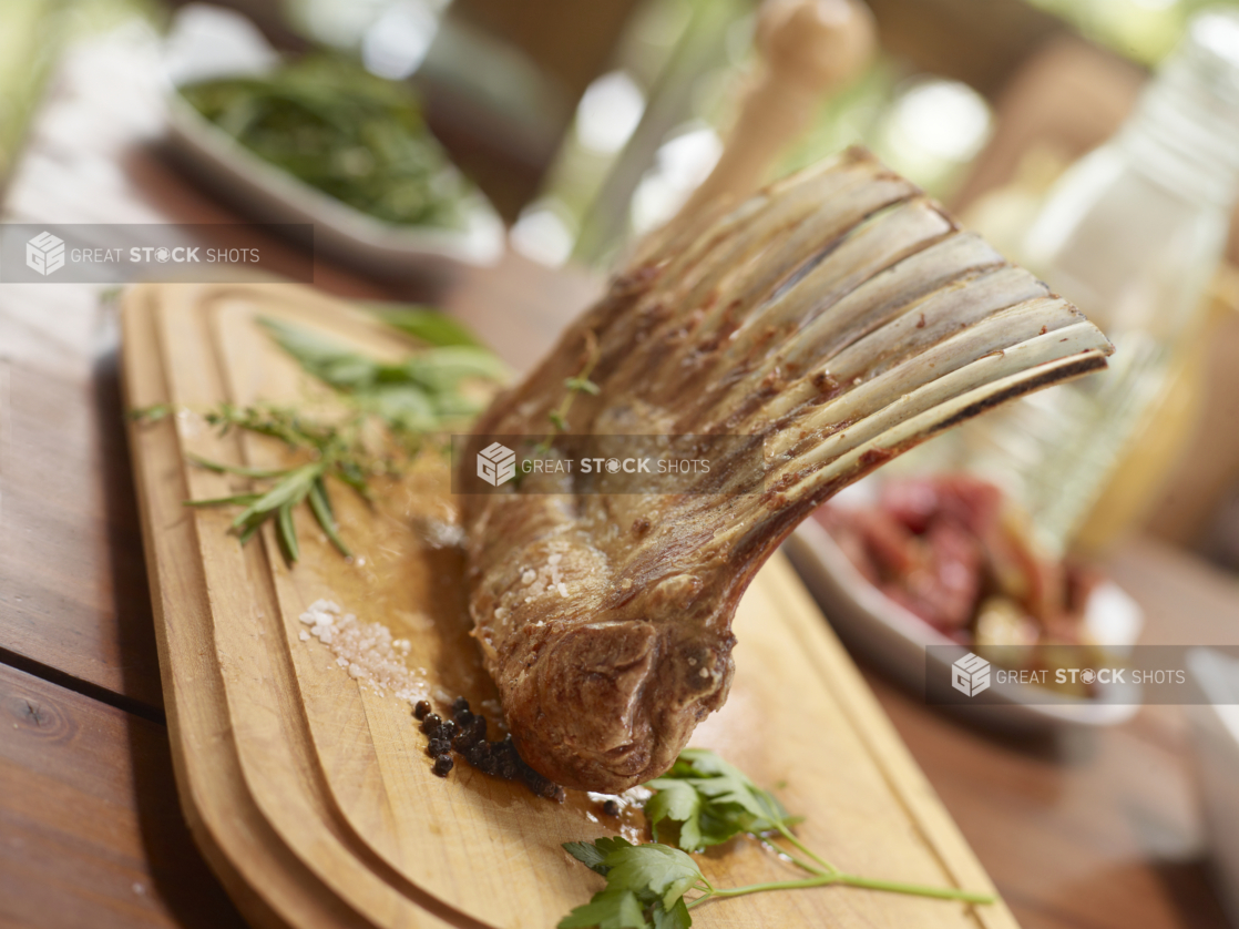 Rack of Lamb on a wood cutting board surrounded by fresh herbs