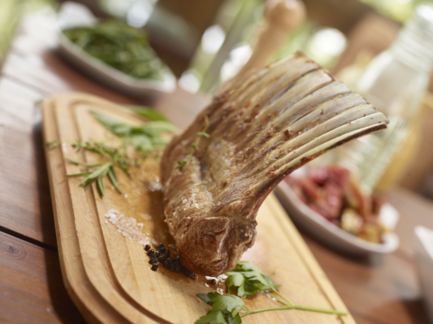 Rack of Lamb on a wood cutting board surrounded by fresh herbs