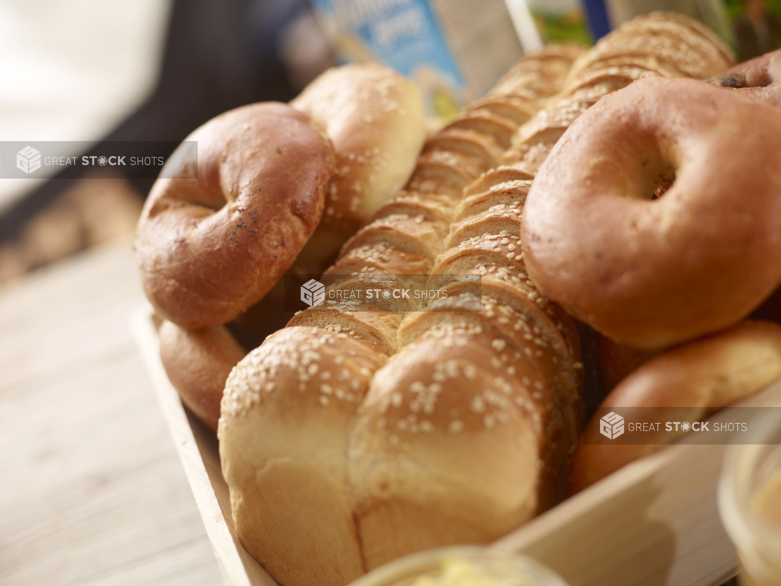 close up of sliced challah loaf with bagels in a wood catering tray