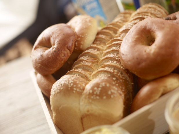 close up of sliced challah loaf with bagels in a wood catering tray