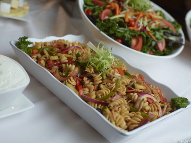 Cold fusilli pasta salad in a rectangular white serving dish, garnished with shredded green onion