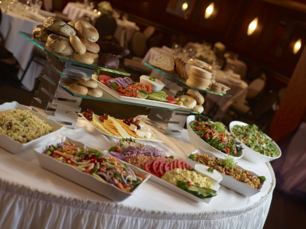 Buffet table at a catered event with dairy platter, lox platter, cheese platter and pasta and other cold salads