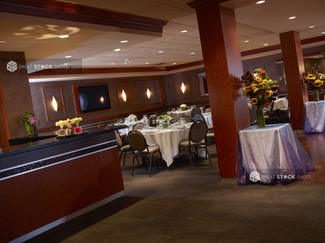 Dining room interior with bar area, empty tables, and tall flower arrangements