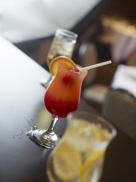 Close Up of a Summery Fruit Cocktail Beverage with an Orange Wedge and Strawberry in a Tall Glass with a Straw in a Restaurant Setting