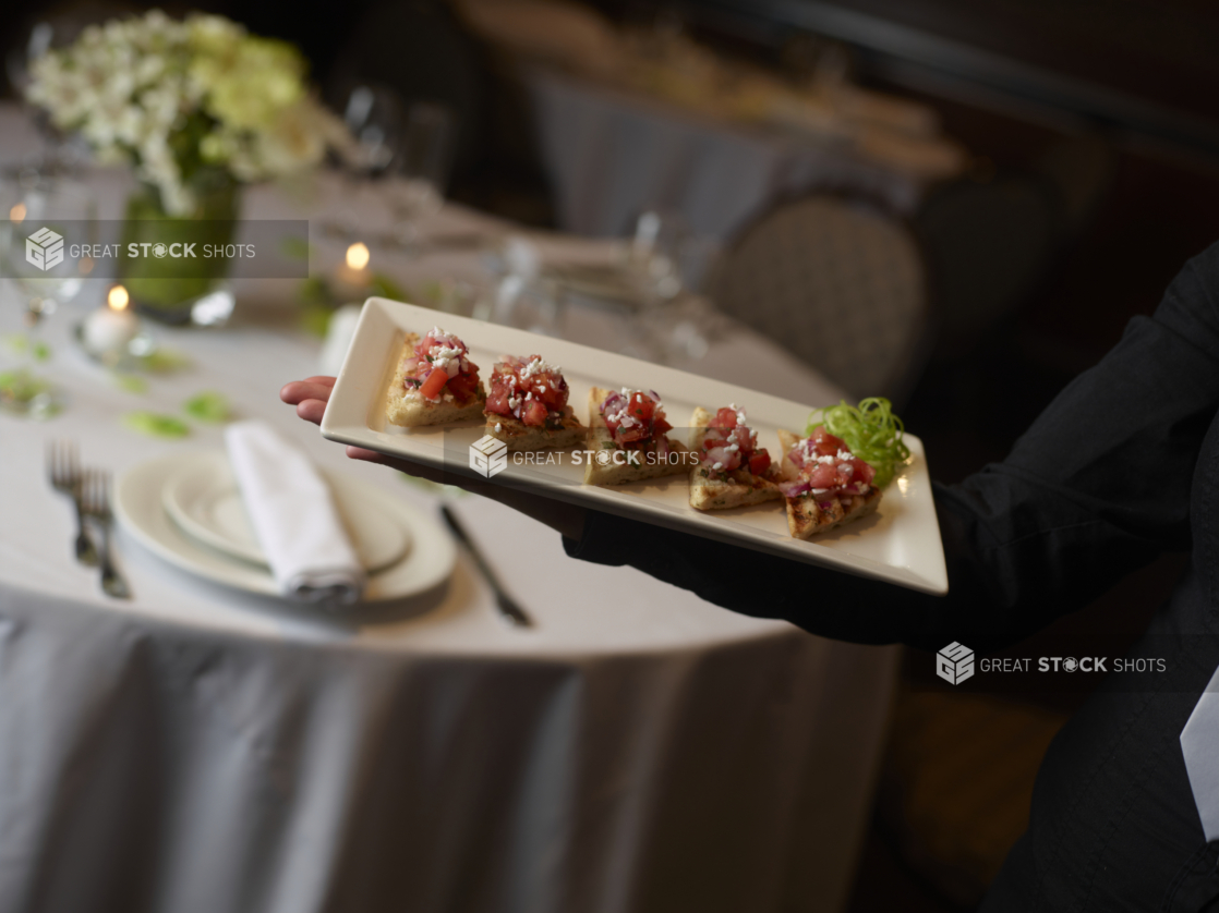 Arm holding a small platter of bruschetta bites at a catered event