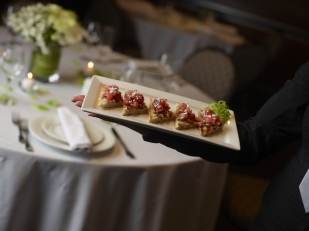 Arm holding a small platter of bruschetta bites at a catered event